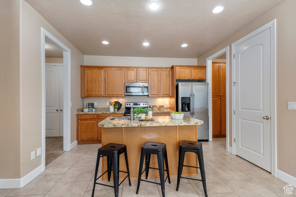 Kitchen with appliances with stainless steel finishes, a kitchen island with sink, light stone countertops, recessed lighting, and a breakfast bar
