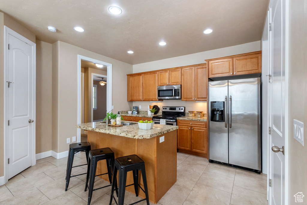 Kitchen featuring stainless steel appliances, a kitchen island, light stone countertops, recessed lighting, and light tile patterned floors