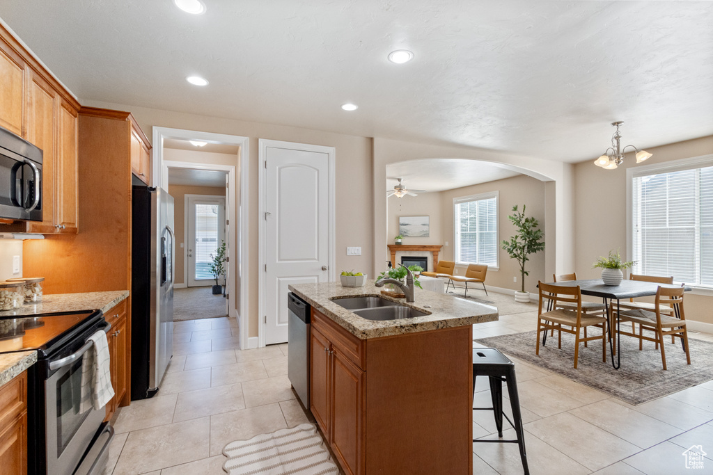Kitchen featuring appliances with stainless steel finishes, a fireplace, a kitchen bar, arched walkways, and light stone counters