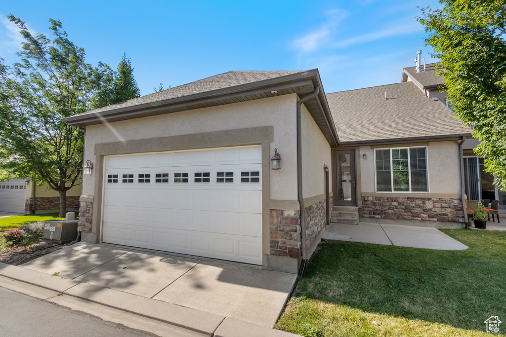 Ranch-style home with stone siding, stucco siding, an attached garage, and a front lawn