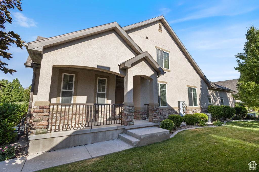View of front of property with stucco siding, stone siding, covered porch, and a front lawn