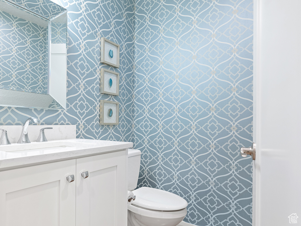Half bathroom featuring wallpapered walls and vanity