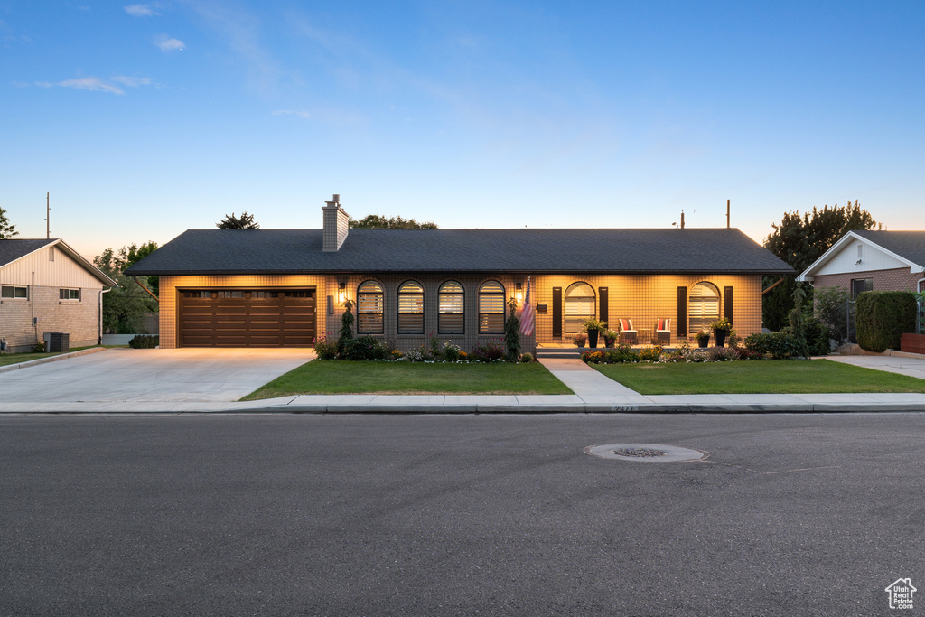 Single story home with concrete driveway, a garage, a chimney, and a front lawn
