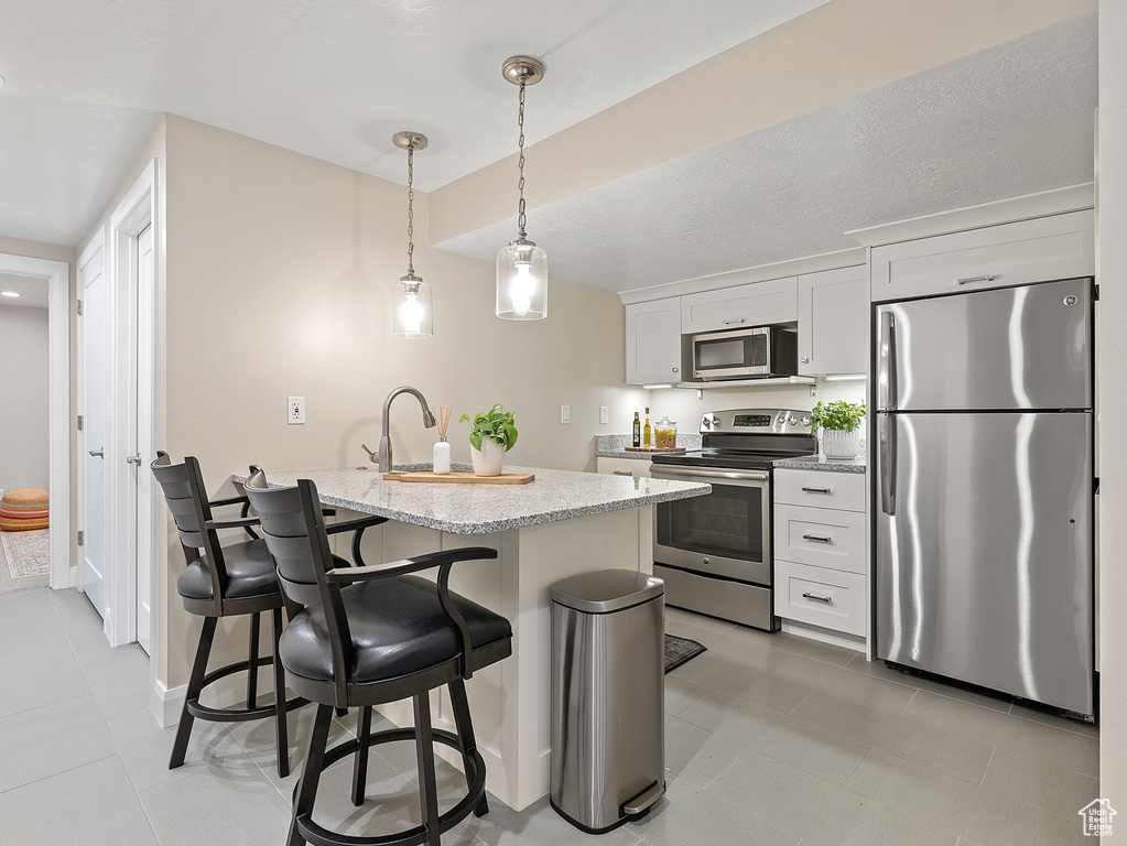 Kitchen featuring stainless steel appliances, a breakfast bar area, white cabinets, hanging light fixtures, and light tile patterned flooring