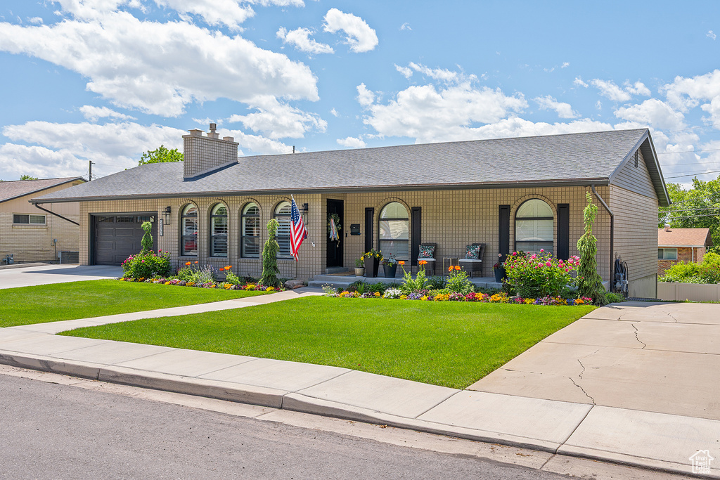 Ranch-style home featuring covered porch, a garage, a front lawn, concrete driveway, and a chimney