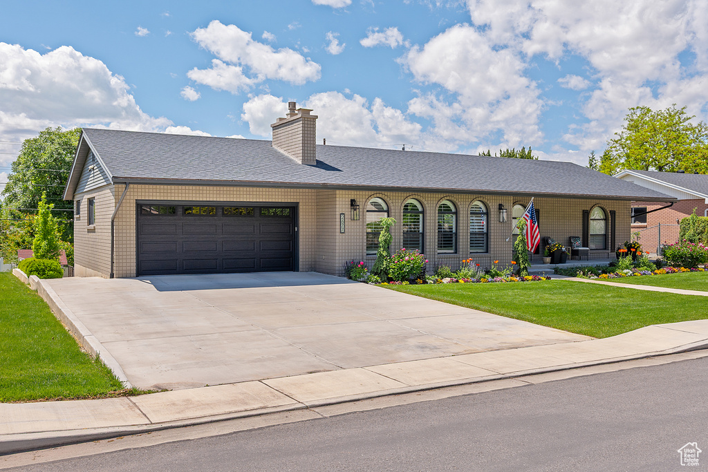 Ranch-style home with a garage, a front yard, concrete driveway, a chimney, and covered porch