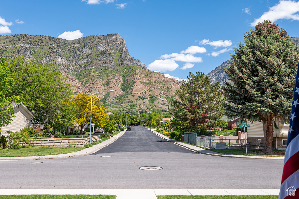View of asphalt road with curbs, a mountain view, street lights, and sidewalks
