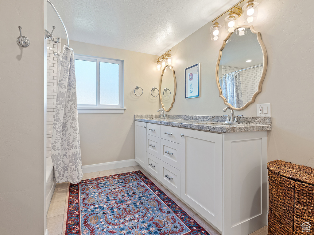 Full bath featuring double vanity, a textured ceiling, and shower / bath combo with shower curtain