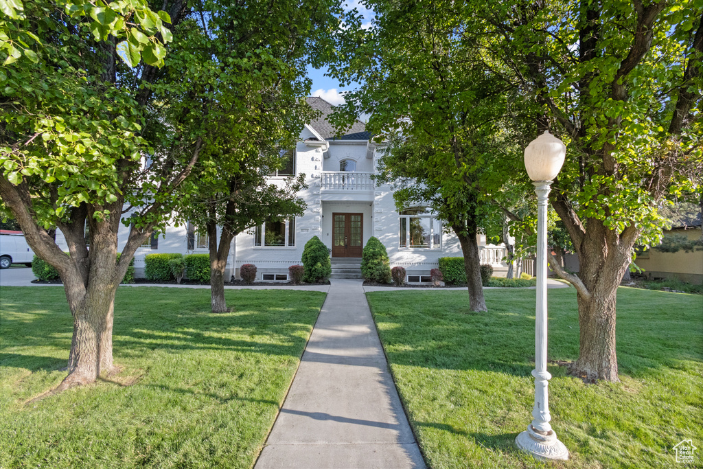 View of property hidden behind natural elements featuring french doors, a front lawn, and a balcony