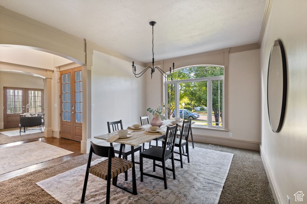 Carpeted dining space with arched walkways, french doors, ornamental molding, and a chandelier