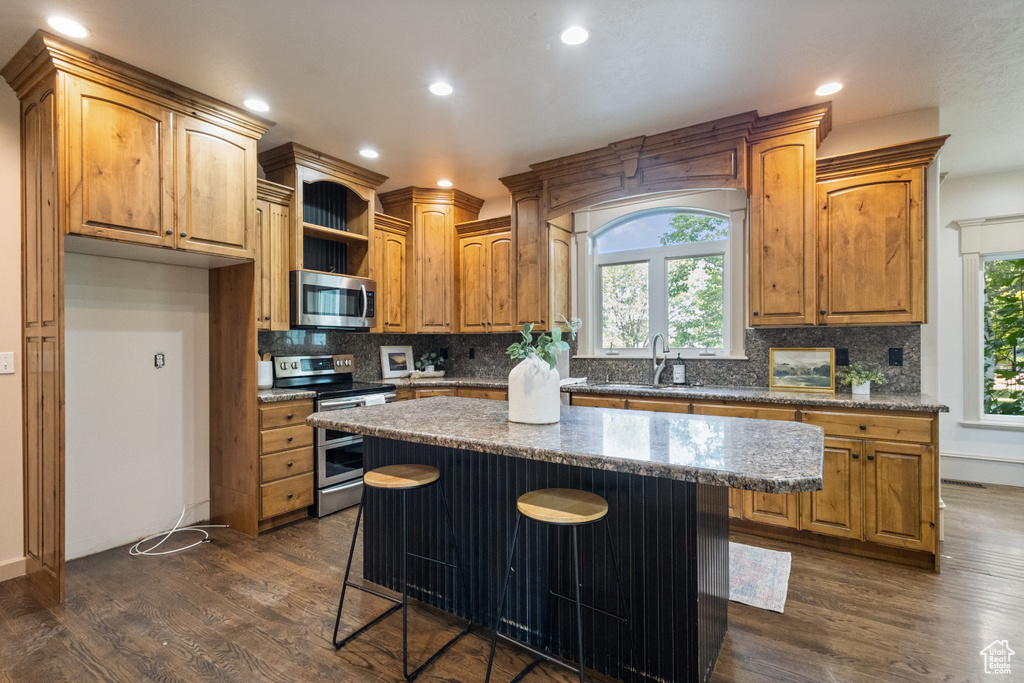 Kitchen featuring stainless steel appliances, dark wood finished floors, backsplash, a center island, and a breakfast bar area