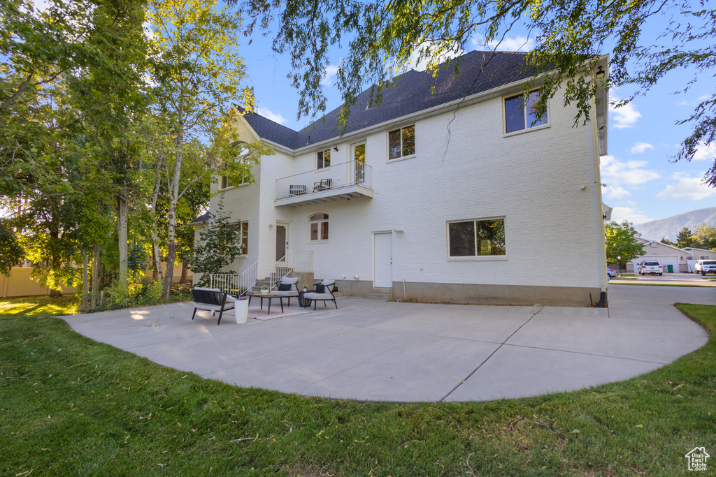 Rear view of house with a balcony, entry steps, a patio, and a yard