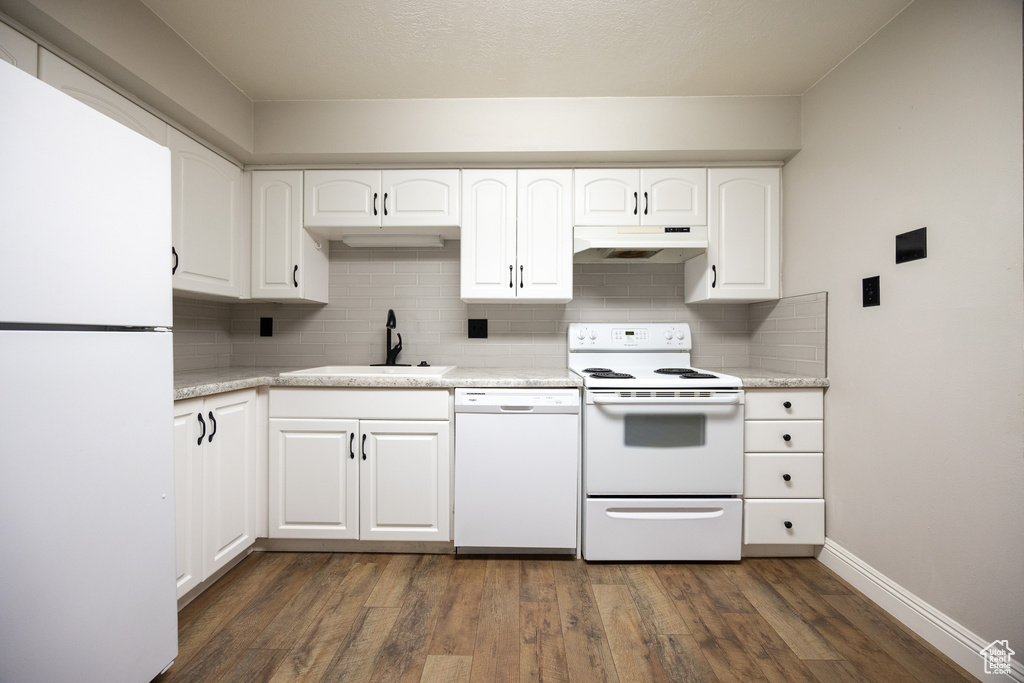 Kitchen with white appliances, under cabinet range hood, decorative backsplash, dark wood-type flooring, and light countertops