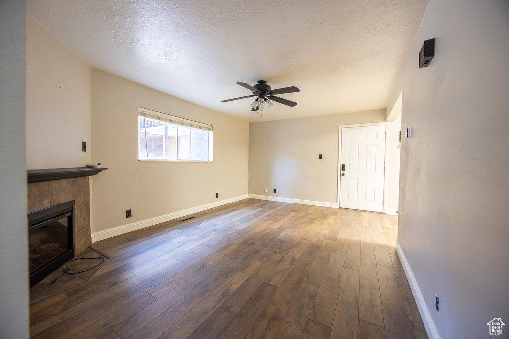 Unfurnished living room featuring hardwood / wood-style flooring, a textured ceiling, ceiling fan, and a fireplace
