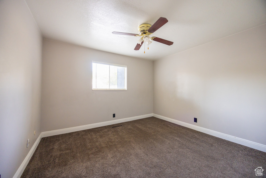 Empty room with dark carpet and a ceiling fan