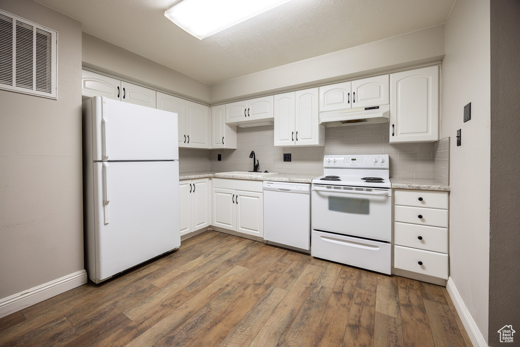 Kitchen with white appliances, under cabinet range hood, hardwood / wood-style flooring, decorative backsplash, and white cabinets