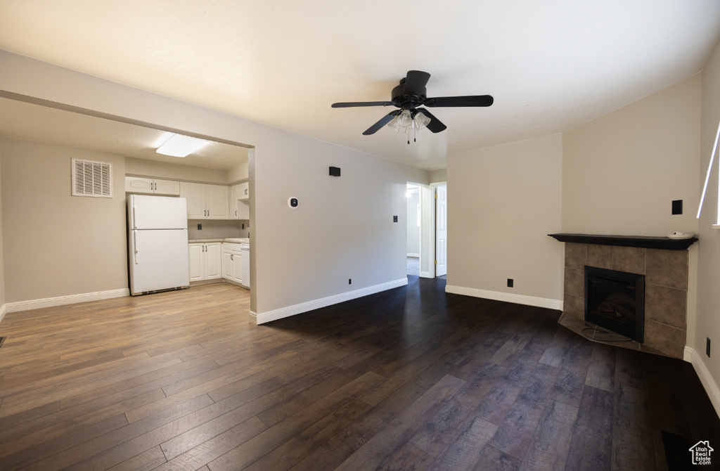 Unfurnished living room featuring dark wood-type flooring, a tile fireplace, and a ceiling fan