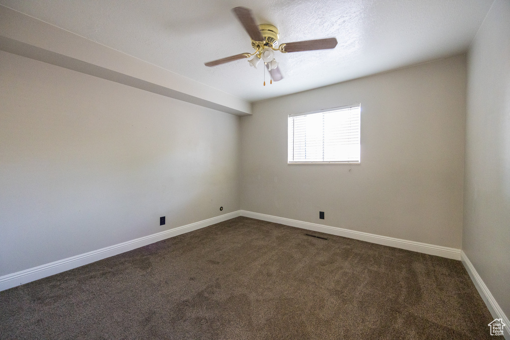 Empty room featuring dark carpet and a ceiling fan