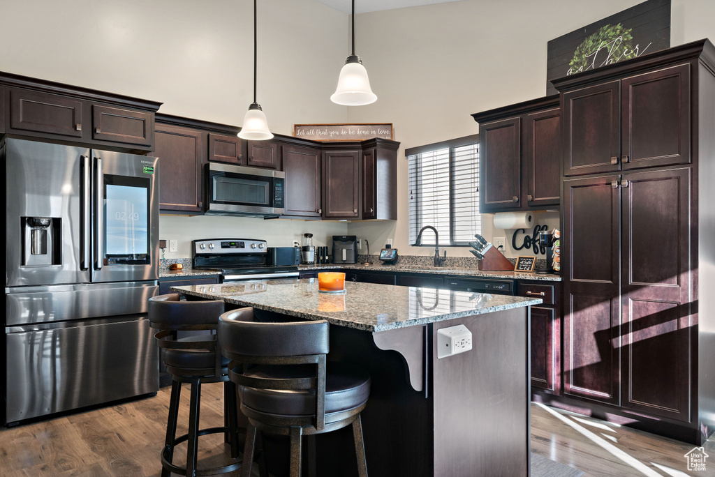 Kitchen with appliances with stainless steel finishes, a high ceiling, dark brown cabinetry, light stone countertops, and a kitchen island