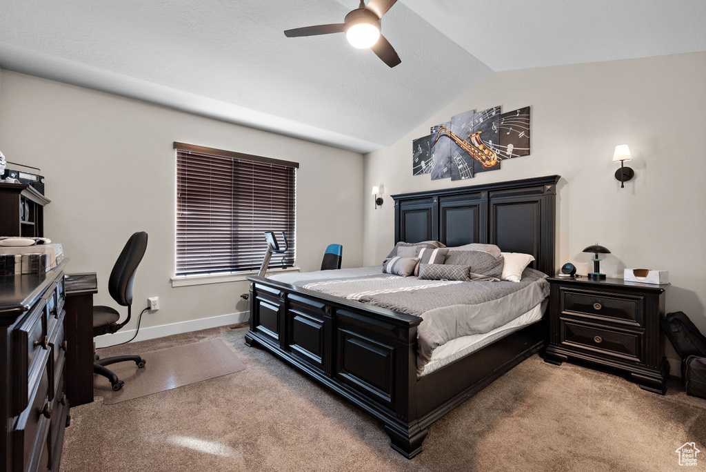 Carpeted bedroom featuring an office area, lofted ceiling, and ceiling fan