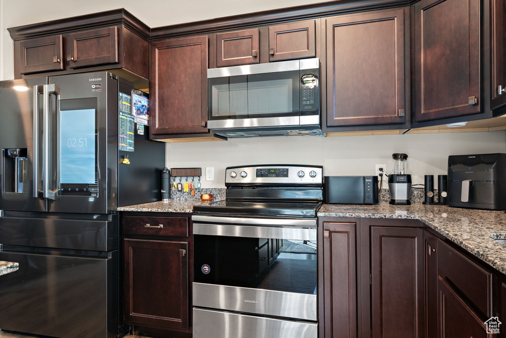 Kitchen with stainless steel appliances, dark brown cabinets, and light stone counters
