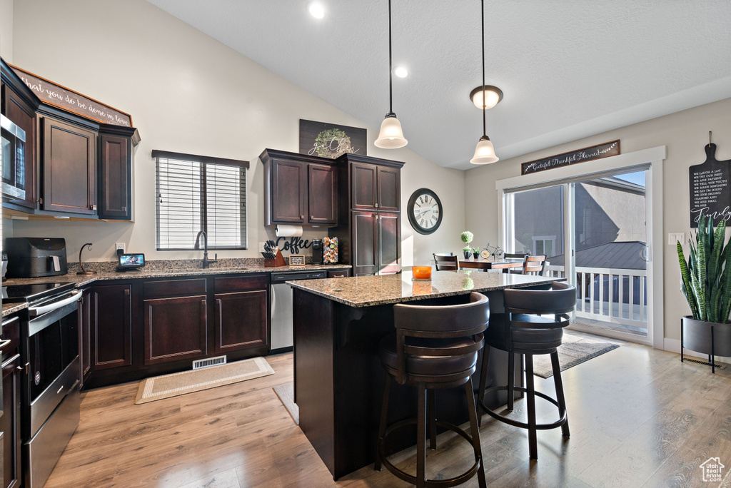 Kitchen featuring appliances with stainless steel finishes, light stone counters, a kitchen island, a kitchen breakfast bar, and dark brown cabinetry