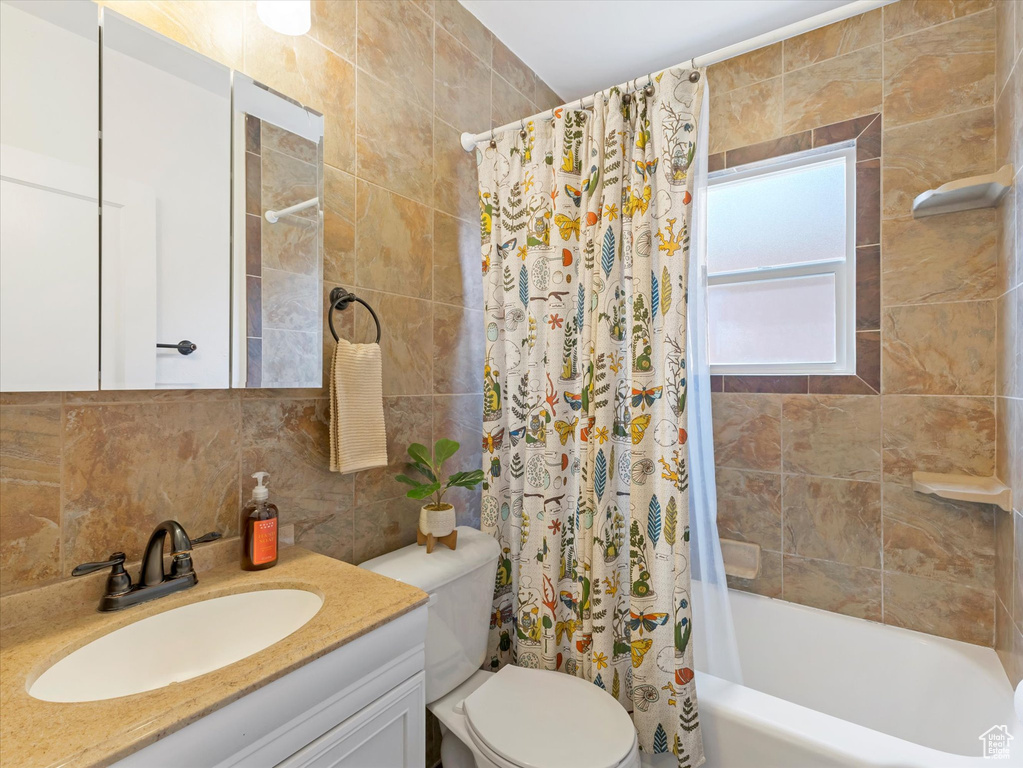 Full bath with decorative backsplash, vanity, shower / bath combo, and tile walls
