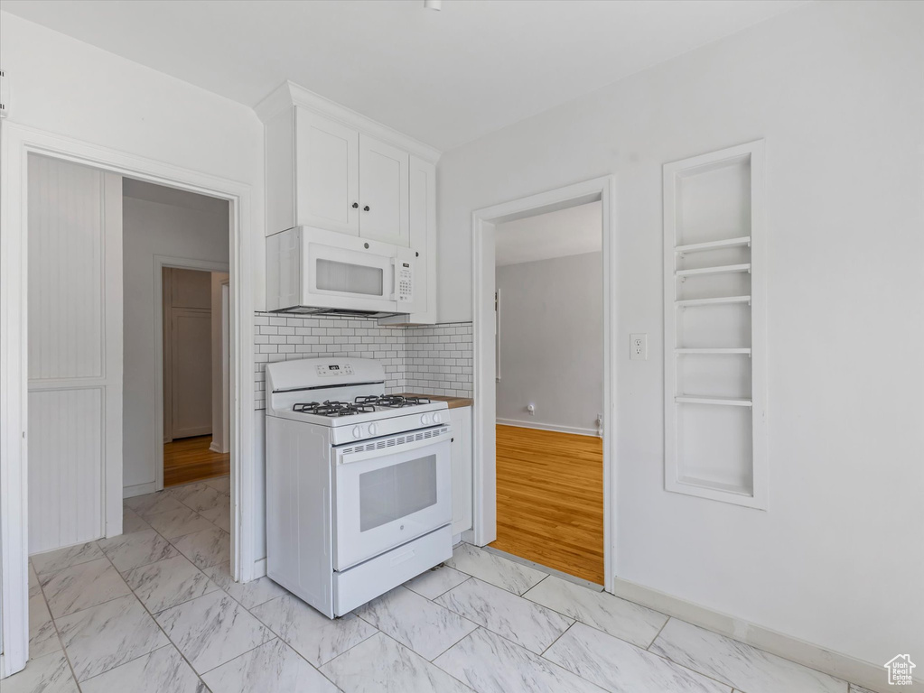 Kitchen featuring white appliances, light marble finish floors, white cabinetry, and backsplash