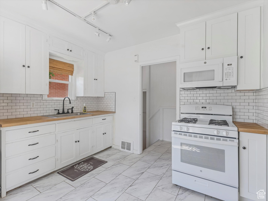 Kitchen with white appliances, wooden counters, white cabinets, light marble finish floors, and tasteful backsplash
