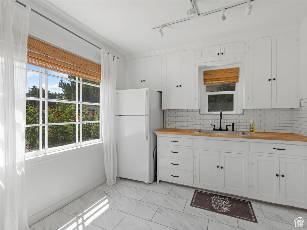 Kitchen featuring freestanding refrigerator, butcher block counters, light marble finish floors, and healthy amount of natural light