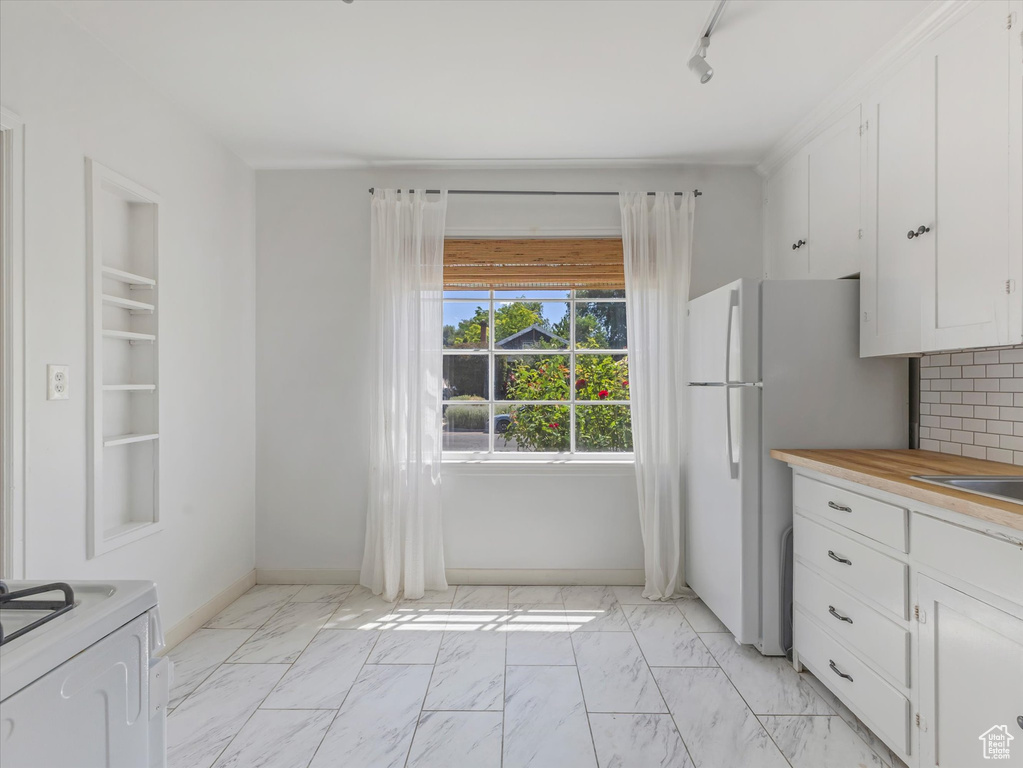 Kitchen featuring light marble finish floors, white cabinetry, freestanding refrigerator, and tasteful backsplash