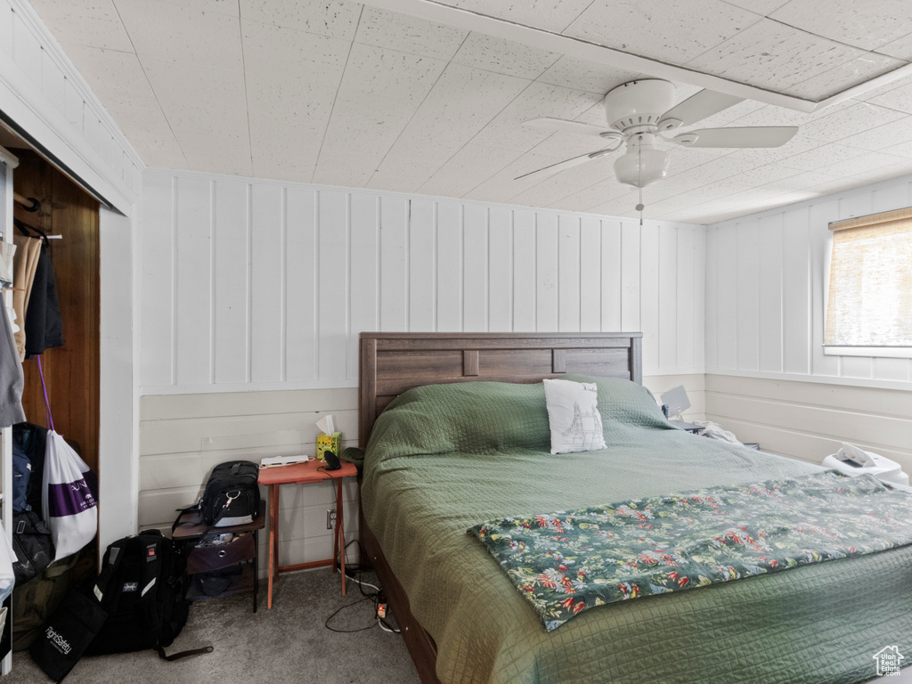 Carpeted bedroom featuring ceiling fan and wood walls