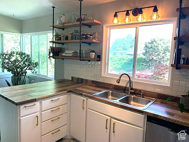 Kitchen with open shelves, stainless steel dishwasher, white cabinets, and healthy amount of natural light