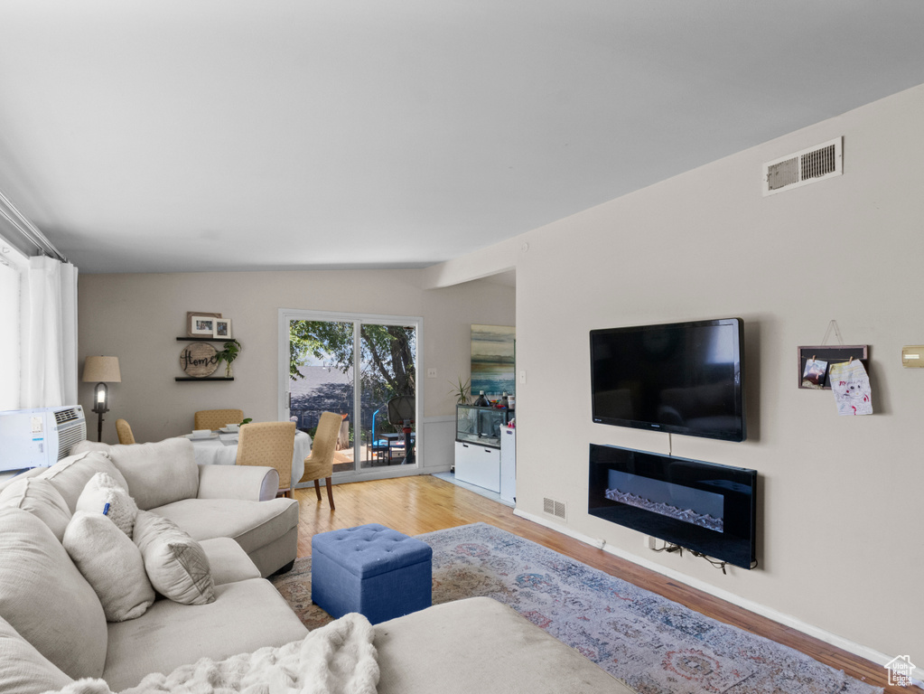 Living area featuring light wood finished floors, vaulted ceiling, and a glass covered fireplace
