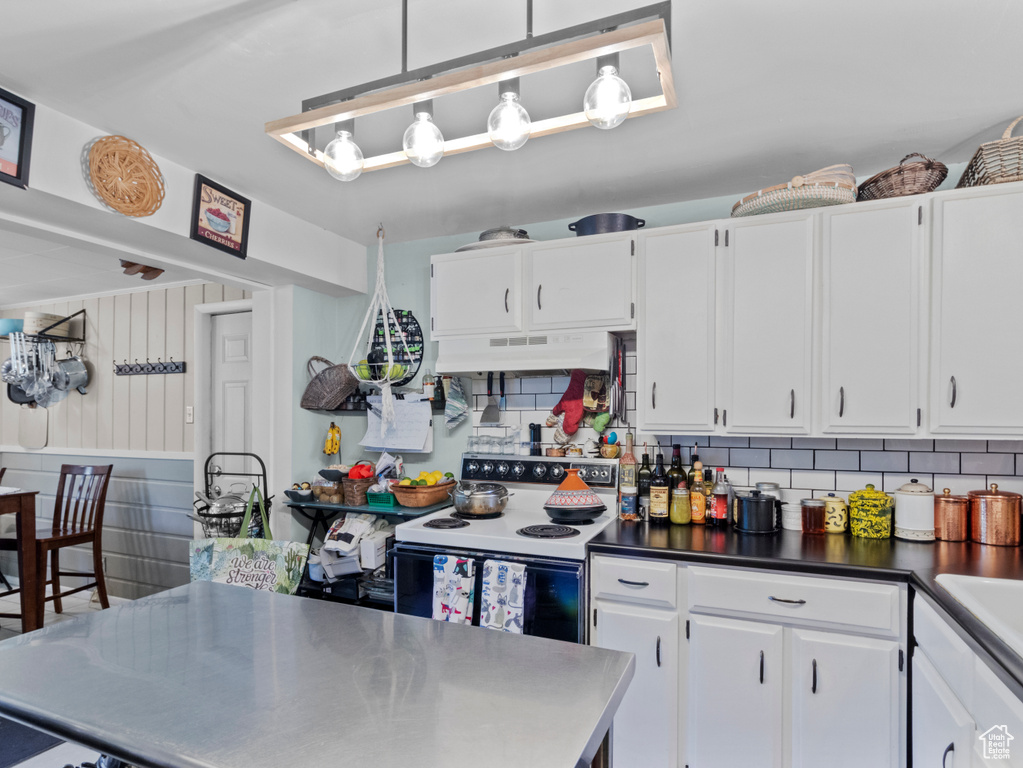 Kitchen featuring electric stove, under cabinet range hood, white cabinetry, and tasteful backsplash