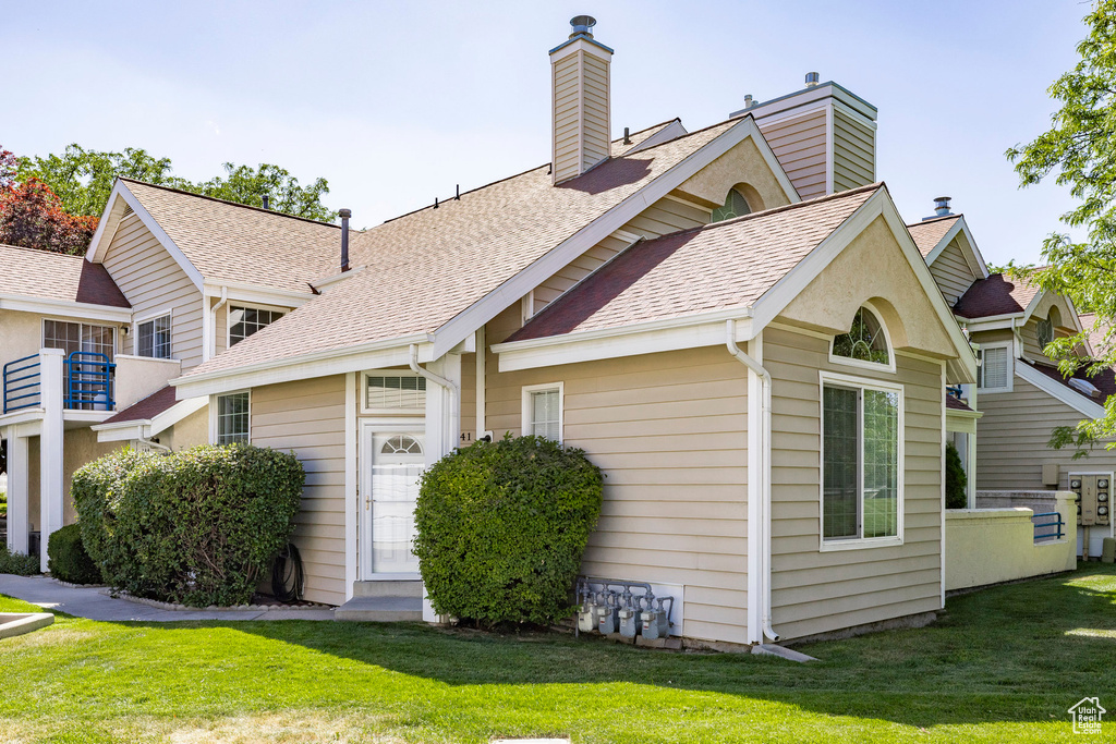 View of front of house featuring a front lawn, a chimney, and a shingled roof