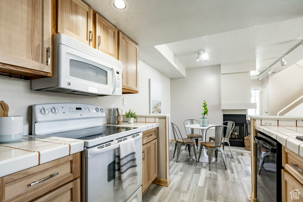 Kitchen with white appliances, tile countertops, rail lighting, light wood-style floors, and a textured ceiling