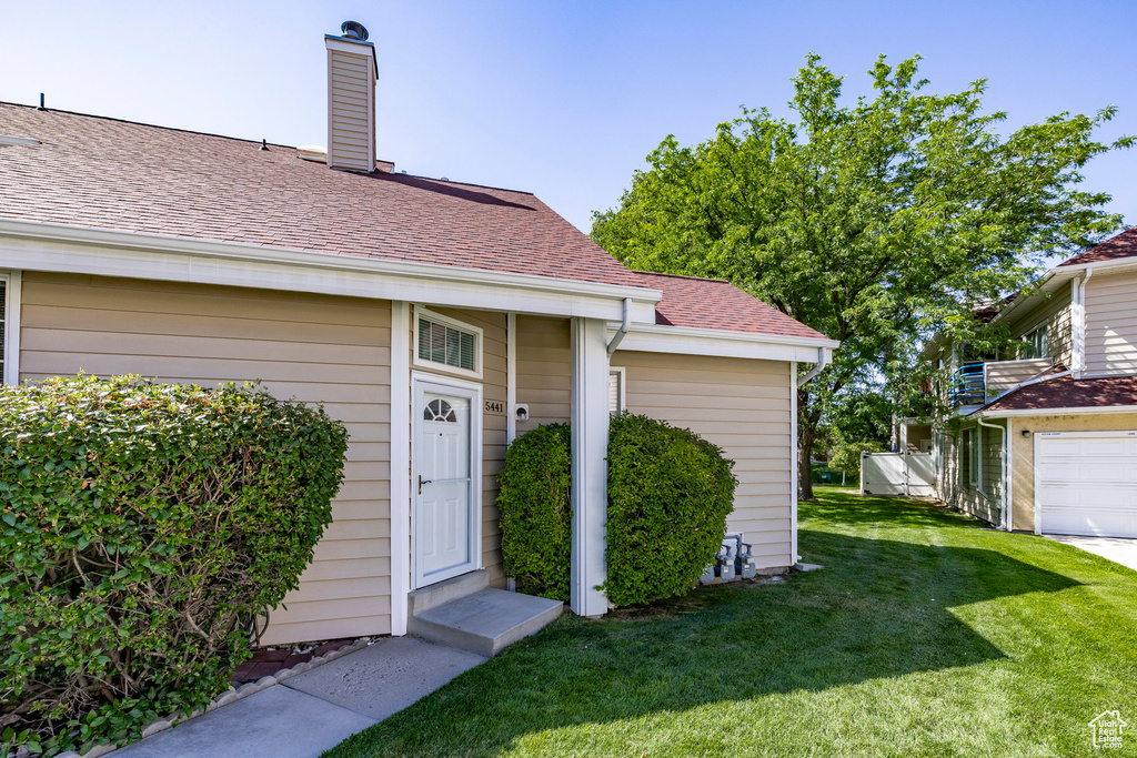 Property entrance featuring a yard, a chimney, a shingled roof, and a garage
