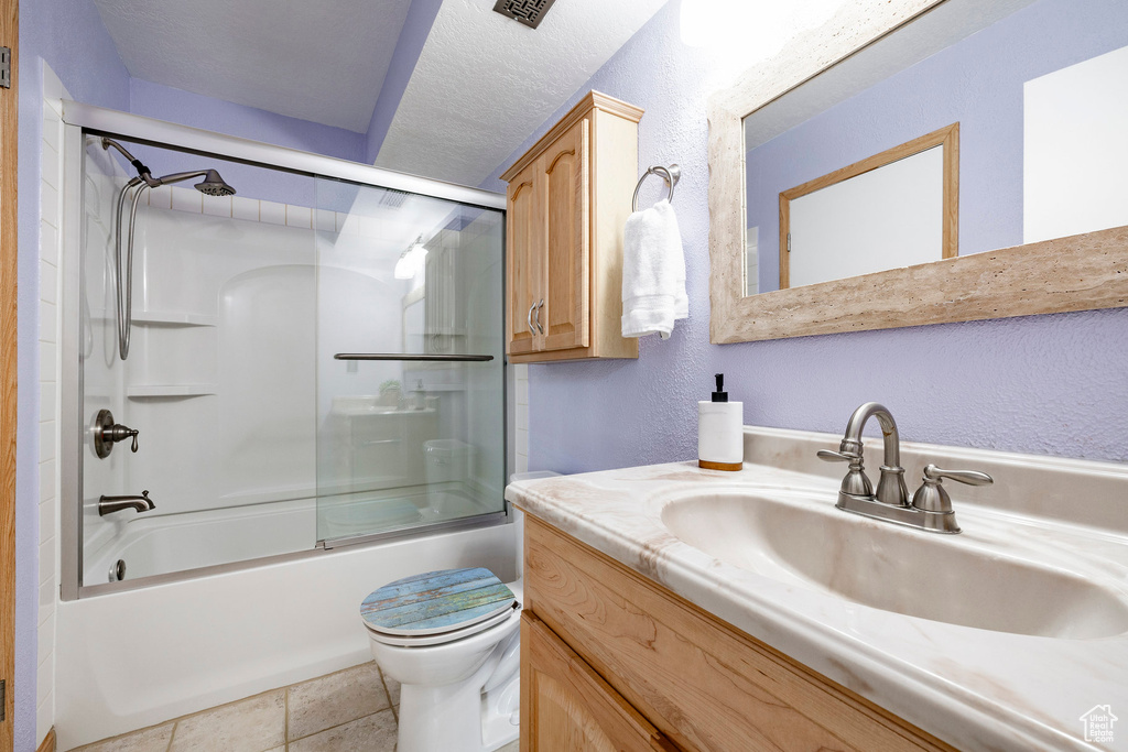 Bathroom featuring vanity, a textured wall, and shower / bath combination with glass door