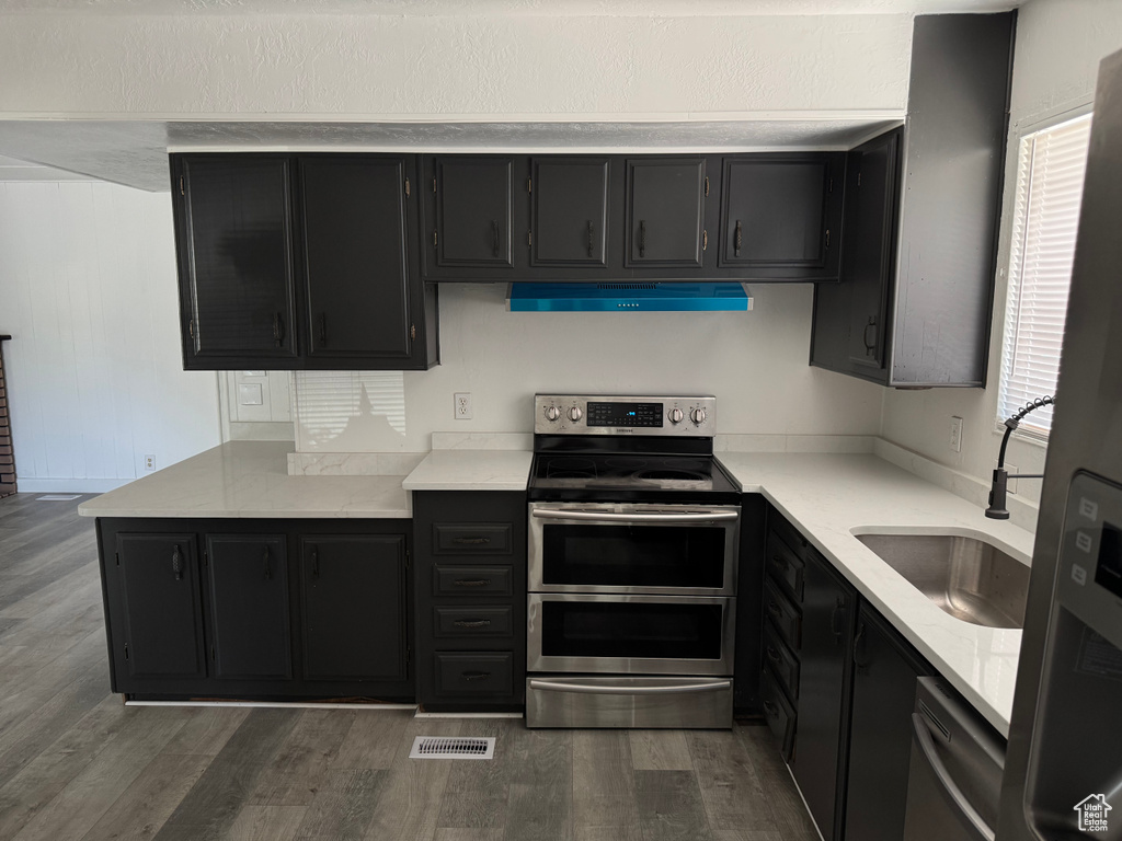 Kitchen with range with two ovens, ventilation hood, dark cabinetry, and dark wood-type flooring