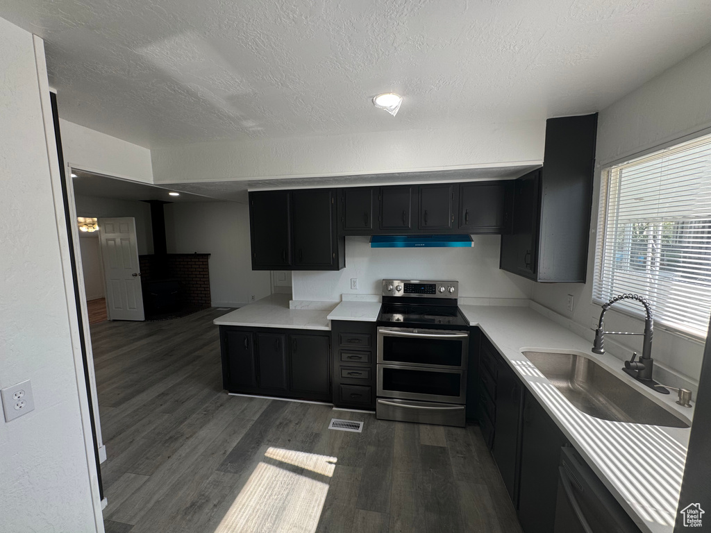 Kitchen featuring double oven range, exhaust hood, dark cabinetry, dark wood-style floors, and a textured ceiling