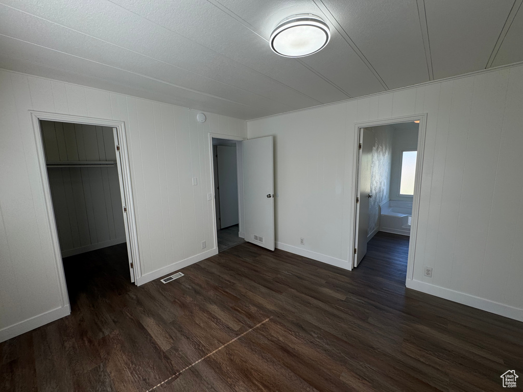 Unfurnished bedroom with dark wood-style floors, a spacious closet, and connected bathroom