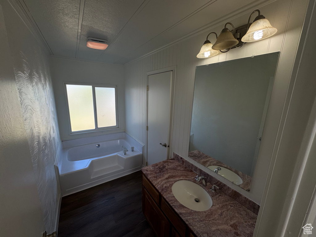 Bathroom featuring a garden tub, vanity, wood finished floors, a textured ceiling, and ornamental molding