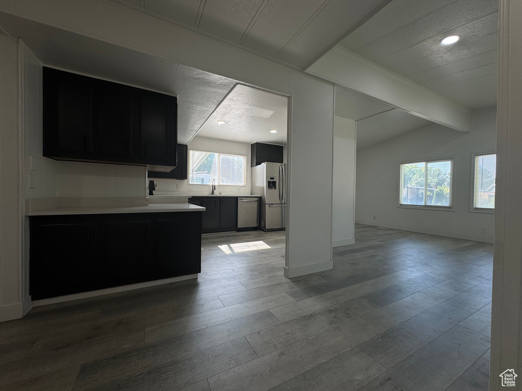 Kitchen featuring stainless steel appliances, dark cabinetry, light countertops, open floor plan, and light wood-type flooring