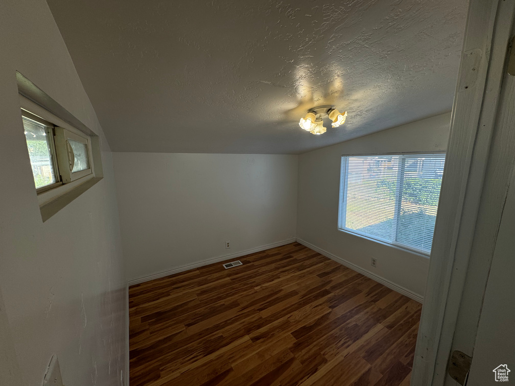 Unfurnished room with vaulted ceiling, a textured ceiling, and dark wood-style flooring