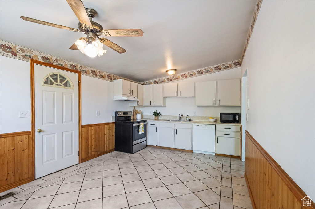 Kitchen featuring white dishwasher, stainless steel range with electric stovetop, a wainscoted wall, black microwave, and under cabinet range hood