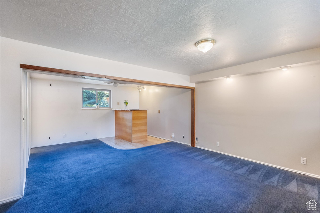 Below grade area with carpet flooring, a textured ceiling, ceiling fan, and bar