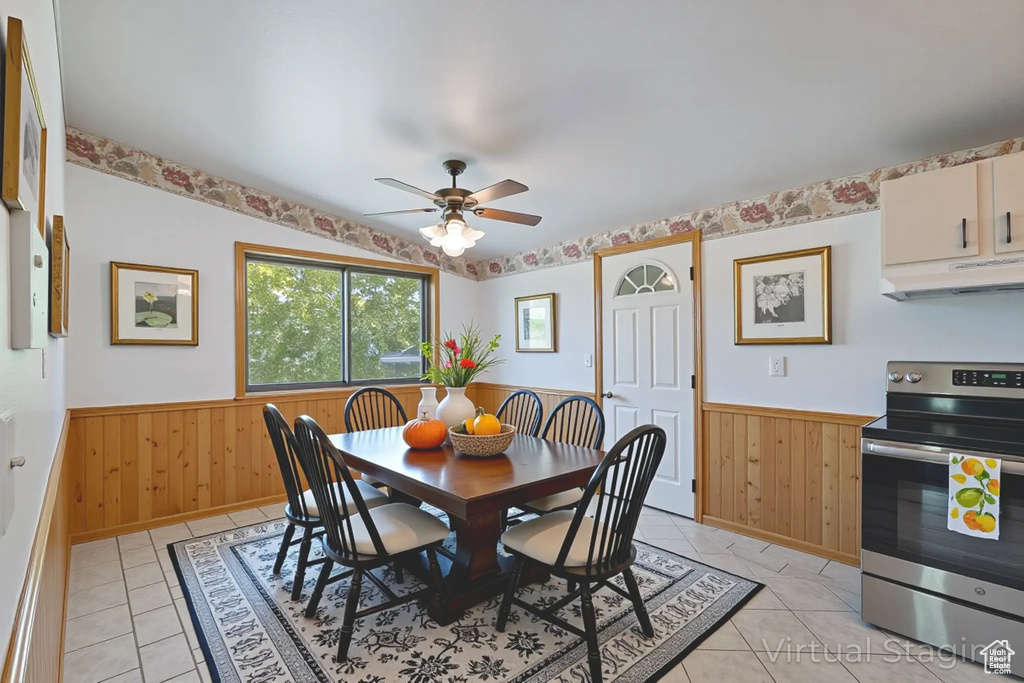 Dining area with a wainscoted wall, ceiling fan, light tile patterned floors, and wood walls