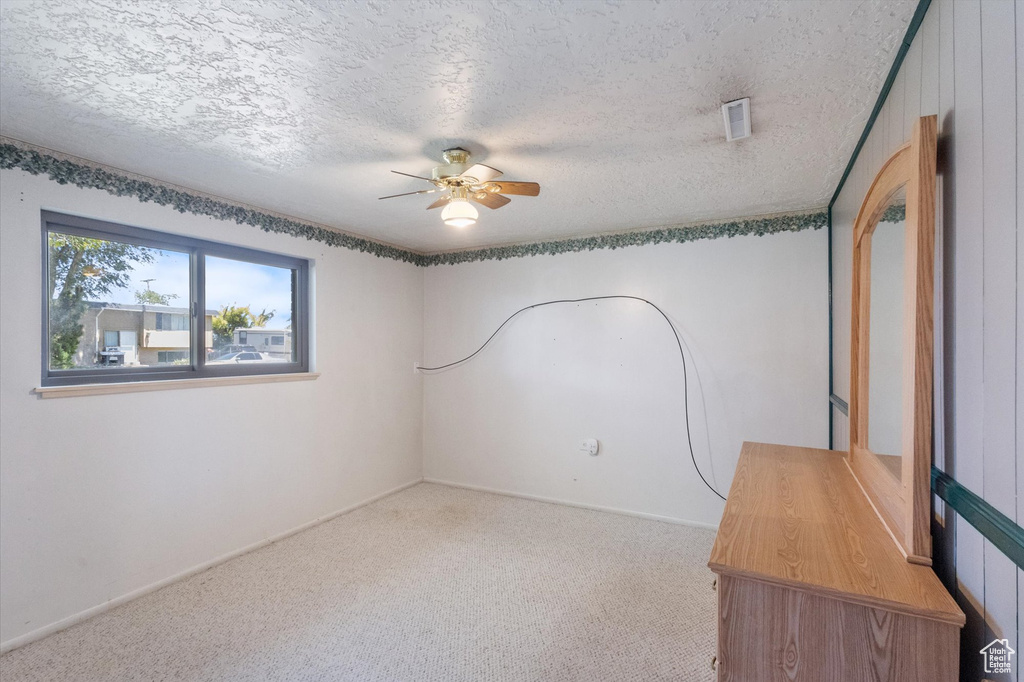 Empty room featuring a ceiling fan, carpet, and a textured ceiling
