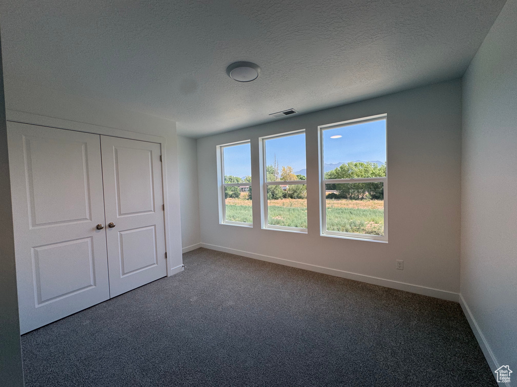 Unfurnished bedroom with dark carpet, a textured ceiling, and a closet
